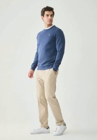 Sweatshirt azul com decote redondo e punhos canelados, combinado com chinos bege claros e ténis brancos. Design simples, ajuste casual.