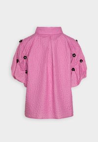 Blusa rosa testurizzata con colletto, maniche corte a sbuffo decorate con accenti floreali neri, caratterizzata da un motivo geometrico su tutta la superficie.