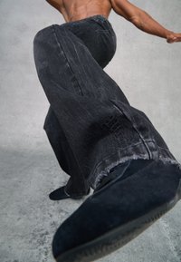 Jeans de mezclilla negra de pierna ancha con una textura deslavada, que presentan un dobladillo desgastado y un detalle de logo bordado cerca del bolsillo.