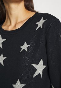 Schwarzer Pullover mit silbernen Sternmustern, Strickstruktur und rundem Ausschnitt. Glitzernde Elemente verleihen dem Design einen besonderen Akzent.