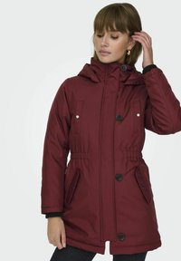 Parka isolée bordeaux avec capuche, taille élastique, poches à boutons-pression et détails de boutons noirs. Extérieur lisse, coupe décontractée.