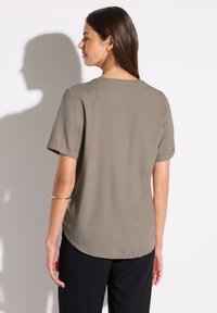 Blusa a maniche corte di colore verde oliva con scollo rotondo, texture morbida e orlo curvo, abbinata a pantaloni neri texture.