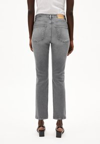 Grå denim jeans med en figursydd midja, utsvängda ben, två bakfickor och en beige läderlapp på midjebandet. Slät textur, minimal detaljering.