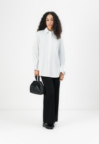 Witte blouse met lange mouwen, gecombineerd met zwarte wijde broek en een kleine zwarte geplooide handtas. Eenvoudig ontwerp en gladde stof.
