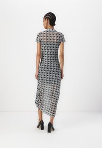 Sheer grey dress with geometric black and white pattern, short sleeves, knee-length hem, and side slits, paired with black high-heeled shoes.