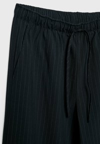Zwarte, gestreepte broek met een elastische tailleband en trekkoord. Bevat zijzakken en heeft een gladde, lichte stoftextuur.