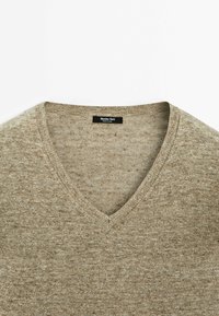 Pull beige en maille avec col en V, texture visible du tissu et étiquette noire Massimo Dutti au col arrière.
