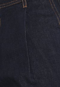 Jeans de mezclilla azul oscuro con costuras naranjas, diseño clásico de cinco bolsillos y una textura suave. La tela es resistente y duradera.