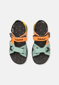 Timberland sandaler med en mintgrønn og oransje fargepalett, justerbare stropper og en svart teksturert såle med et sekskantet mønster.
