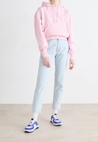 Sudadera corta rosa con un bolsillo frontal, combinada con jeans rectos de corte ligero en azul claro y zapatillas blancas y azules. Tejido en mezcla de algodón.