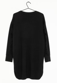 Schwarzes Langarmkleid mit rundem Halsausschnitt, das Rüschendetails an den Ärmeln und einen geschwungenen Saum aufweist, der an den Seiten verlängert ist.