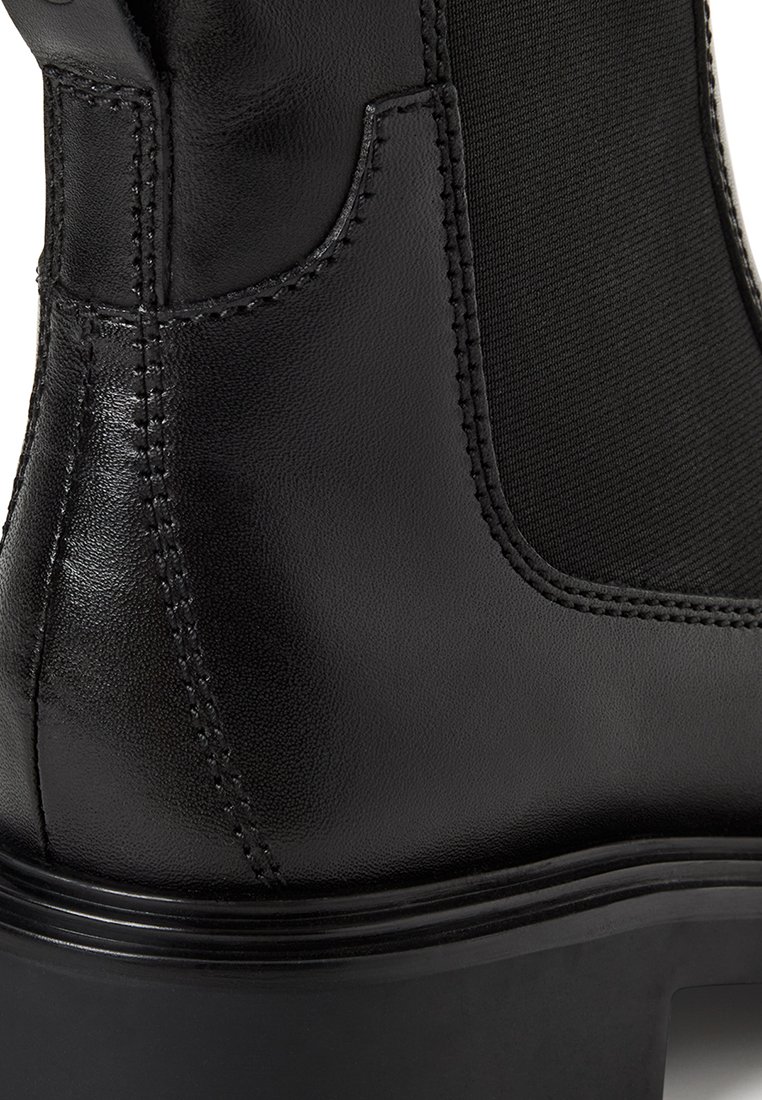 Zwarte enkellaars met een bovenwerk van glad leer en elastische zijpanelen. Voorzien van stiksels en een chunky, gestructureerde zool voor stabiliteit.