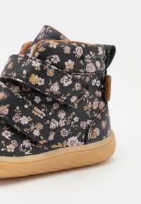 Černé boty s květinovým vzorem a suchým zipem, vybavené polstrovaným límcem, gumovou podešví a textilními detaily v růžové a zlaté barvě.