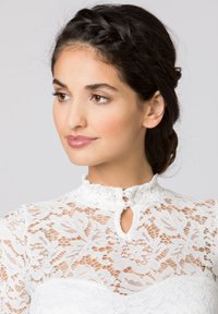 Weißes Spitzenbluse mit hohem Kragen, verziert mit aufwändigen floralen Mustern und einer Schlüssellochöffnung, die mit zwei dekorativen Knöpfen gesichert ist.