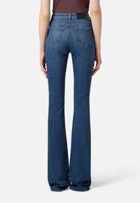 Jeans a vita alta a zampa d'elefante in denim blu scuro, caratterizzati da una texture liscia, tasche posteriori e un'etichetta nera del marchio sulla vita.