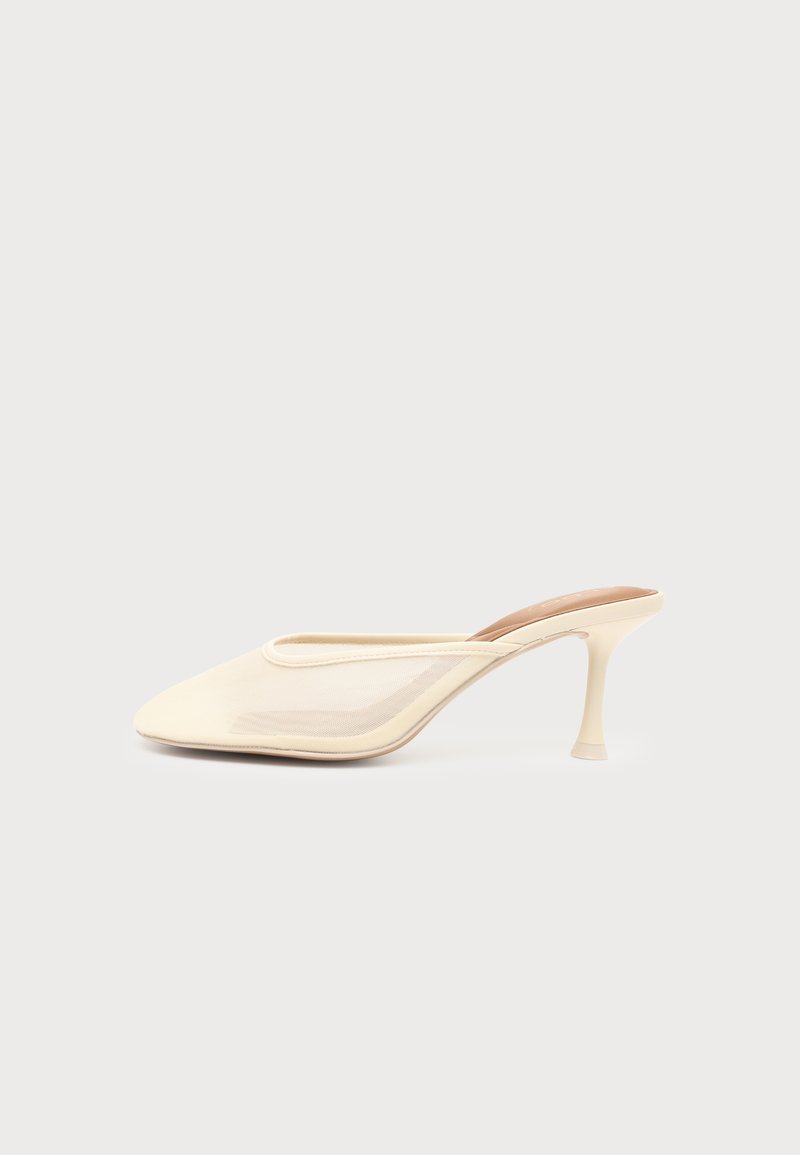Mule à talons hauts couleur crème avec bout pointu et panneaux latéraux en mesh, présentée sur un fond clair uni.