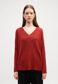 Czerwony sweter z prążkowanego materiału z dekoltem w serek, długimi rękawami i luźnym krojem. Teksturowany materiał w jednolitym kolorze, bez wzorów i ozdób.