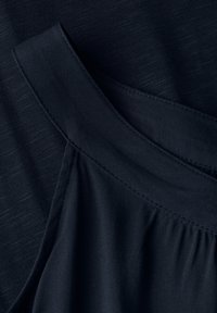 Tmavě námořnická látka s hladkou texturou, sevolným střihem a nabíraným detailem na švu. Lehký a neformální design.