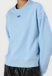 Jasnoniebieska bluza z bawełny z dodatkiem włókien syntetycznych, z okrągłym dekoltem, ściągaczami przy mankietach oraz małym, niebieskim logo "HUGO" na piersi.