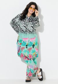 Blusa a fantasia con macchie di leopardo in bianco e nero che sfumano in un degradé teal, abbinata a pantaloni floreali coordinati e sandali metallici.