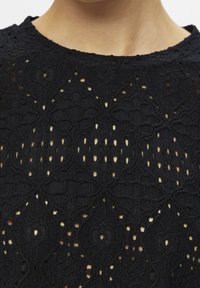 Haut en tricot noir présentant un motif complexe avec des détails en ajouré, un tissu texturé et un col rond.