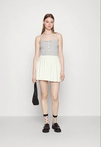 Striped tank top with buttons, paired with a pleated white skirt. Black platform shoes and heart-patterned socks. Black handbag.