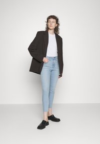 Blazer escuro oversized sobre uma t-shirt branca, combinado com jeans skinny de tom azul claro e sapatos pretos slip-on. Visual simples e moderno.
