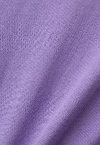 Gros plan sur un tissu tricoté doux de couleur lilas avec des mailles fines et régulières, et des plis subtils créant une texture.