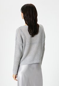 Maglione grigio chiaro lavorato a maglia con texture a coste, dal design leggermente accorciato e maniche lunghe. Indossato sopra una gonna in satin argento liscia.