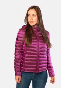 Doudoune légère violette avec texture matelassée horizontale, fermeture éclair sur le devant et capuche. Présente un logo noir rond sur la manche.