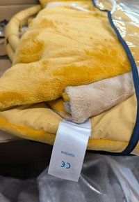 Yellow and cream plush blanket with a soft texture, featuring a stitched edge and a care label. Partially folded, showing both colors.
