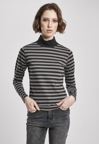 Stribet turtleneck top i grå og sort med lange ærmer, fremstillet i et blødt materiale og en tætsiddende pasform. Båret med mørke jeans.