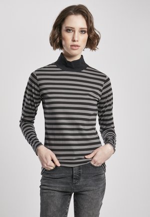 Striped turtleneck top in gray and black with long sleeves, featuring a soft fabric and form-fitting design. Worn with dark jeans.