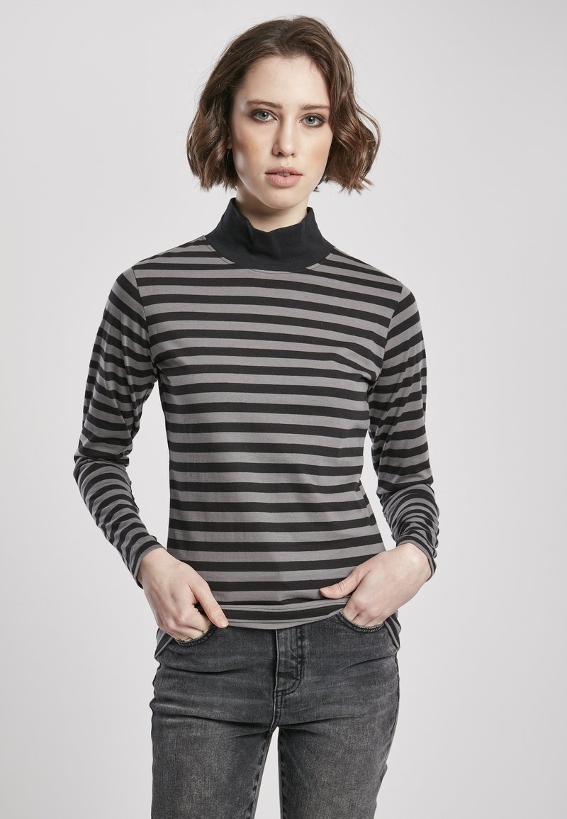 Stribet turtleneck top i grå og sort med lange ærmer, fremstillet i et blødt materiale og en tætsiddende pasform. Båret med mørke jeans.