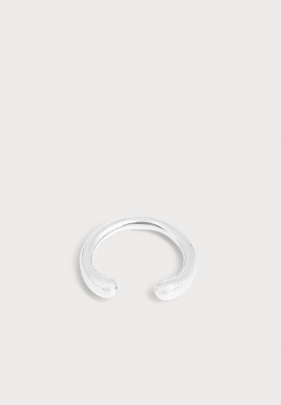 Bracelet manchette en argent lisse et ouvert avec des extrémités arrondies, présenté sur un fond gris clair uni.