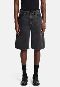 Shorts in denim nero con una vestibilità ampia, lunghezza a metà coscia, design a cinque tasche e cuciture a contrasto. Indossati con calze nere e mocassini.
