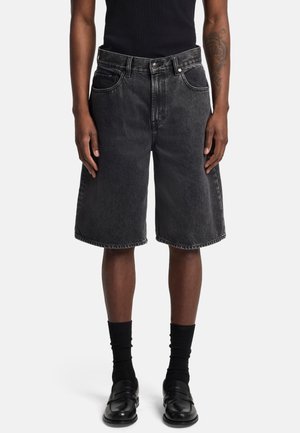 Zwarte denimshorts met een losse pasvorm, halve-dij lengte, vijf zakken en contrasterende stiksels. Gestyled met zwarte sokken en loafers.