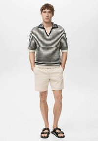 Stribet strik polo i sort og hvid, kortærmet, V-hals, parret med beige shorts og sorte sandaler. Flad tekstur, afslappet design.