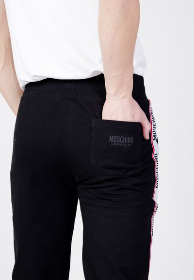 Czarne bawełniane spodnie dresowe mają tylną kieszeń z subtelnym wytłoczonym logo, akcentowane boczną paskiem z nazwą marki w kolorze różowym.