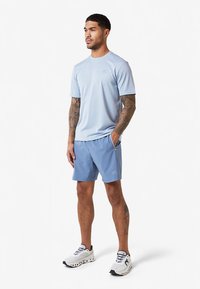 Lichtblauw atletisch T-shirt met korte mouwen, gecombineerd met bijpassende blauwe shorts. Kenmerken zijn subtiele branding en een lichtgewicht stof.