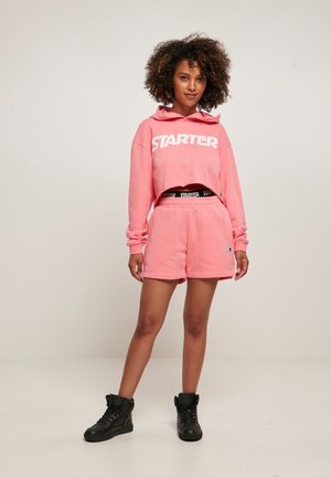 Pink cropped hoodie with large white "STARTER" logo, paired with matching shorts and black high-top sneakers, featuring a relaxed design.