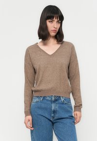 Maglione marrone a V con maniche lunghe, orlo a coste, texture morbida, indossato con jeans in denim blu a vita alta.