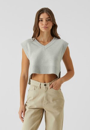 Pull court gris clair à col en V et manches courtes, avec un ourlet côtelé. Porté sur un pantalon beige taille haute, modèle posant de face.
