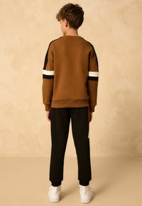 Brauner Hoodie mit schwarz-weißen Streifendetails; kombiniert mit schwarzen Hosen. Baumwollmischung, lockere Passform und gerippte Bündchen und Saum.