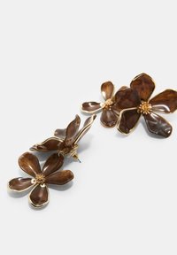 Bruna blommiga örhängen med glansiga kronblad och guldfärgade detaljer, med en texturerad mitt som liknar små pärlor.