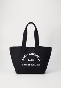 Black tote bag made of canvas featuring white printed text: "KARL LAGERFELD," "PARIS," and "21 RUE ST-GUILLAUME." Dual flat handles.