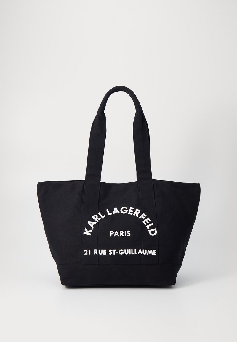 Black tote bag made of canvas featuring white printed text: "KARL LAGERFELD," "PARIS," and "21 RUE ST-GUILLAUME." Dual flat handles.