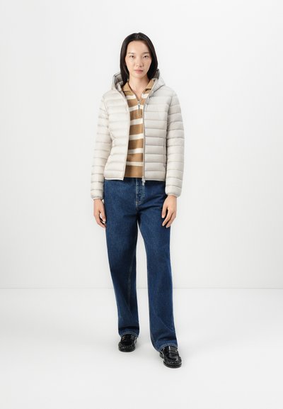 Doudoune gris clair avec capuche, dotée d'une fermeture éclair à l'avant et d'un design matelassé horizontal, portée sur un haut en tricot rayé marron et un jean bleu.