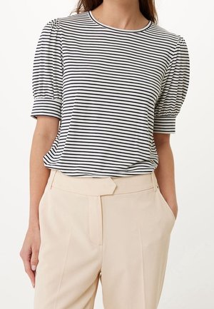 Kobieta ubrana w czarno-biały top z bufkowymi rękawami w paski, włożony w beżowe spodnie z wysokim stanem z unikalnym paskiem w talii.