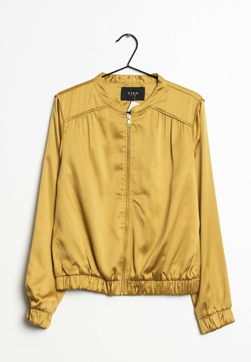 Veste bomber en satin jaune moutarde avec fermeture éclair à l’avant, poignets et ourlet élastiques, suspendue sur un cintre noir contre un fond blanc.